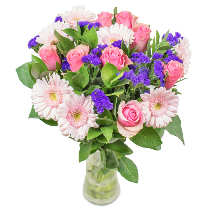 A radiant bouquet artfully arranged in a clear glass vase, photographed against a pristine white backdrop-this is a showpiece embodying the creative spirit of Whitechapel's local florists. At its heart, 7 to 9 medium and pale pink roses, many still in bud or only just opening to reveal tightly wound petals, demonstrate classic spiral beauty and impeccable freshness. Intertwined among them are 5 to 7 large-headed blush gerbera daisies, each with a corona of gently fanned petals and almost white centers, lending a sense of gentleness and poise. Clusters of deep purple statice, identifiable by their vivid colour and delicate structure, punctuate the arrangement with vibrant energy and unexpected dimension. Generous, deep green foliage envelops the lower stems, imbuing the bouquet with vitality and a sense of natural abundance. Through the vase's transparency, water glimmers against intertwining stems, suggesting a just-delivered freshness from a nearby Whitechapel market. Ideal for birthdays along Cable Street, heartfelt tributes for Mother's Day, or as a refined statement piece for a Whitechapel flat, this arrangement of roses, gerberas, and statice communicates feelings of joy, celebration, and thoughtful affection with every detail.